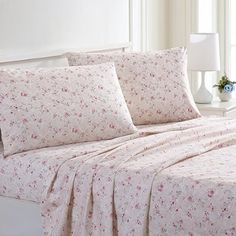 a white bed with pink flowers on it in a room next to a lamp and window