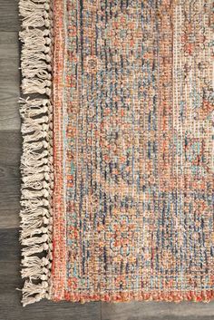 an orange, blue and white rug with fringes on the bottom is laying on a wooden floor