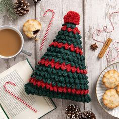 a knitted christmas tree ornament next to cookies and cup of coffee on a table