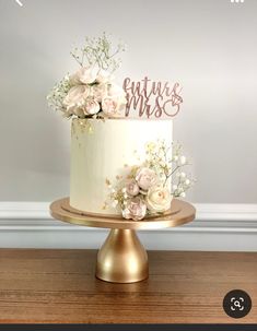 a white cake with pink flowers and the words future mrs on top is sitting on a gold plate