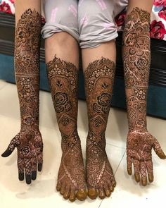 the legs and feet of a woman with henna tattoos on their hands, both covered in intricate designs