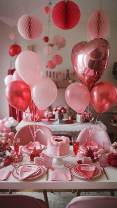 a table topped with lots of pink and red heart shaped balloons next to a cake