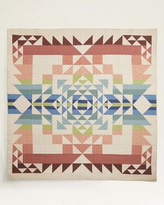 a colorful quilt hanging on the wall next to a white wall with a wooden frame