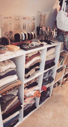 a woman standing in front of a white shelf filled with lots of clothes and jewelry