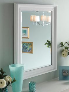 a bathroom mirror sitting on top of a counter next to a vase and candle holder