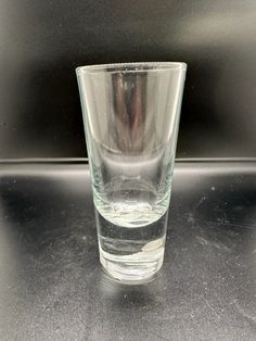 a clear glass sitting on top of a table next to a black counter with a silver object in the background