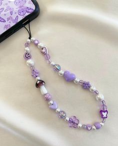 a purple and white beaded necklace next to a cell phone on a bed with butterflies