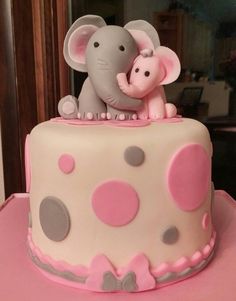 a pink and gray polka dot cake with an elephant figurine sitting on top