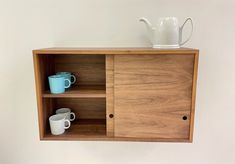 a wooden cabinet with two mugs and a teapot on it's shelf