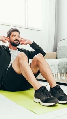 a man sitting on top of a green mat in front of a couch holding his hands to his ears