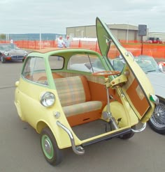 an old yellow car with its door open in a parking lot next to other cars