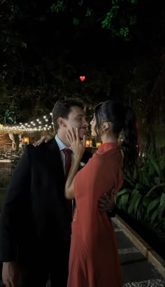 a man and woman standing next to each other in front of some trees at night