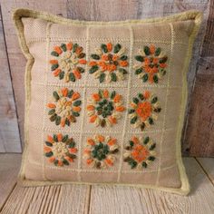 an embroidered pillow with orange and green flowers on the front, sitting on a wooden surface