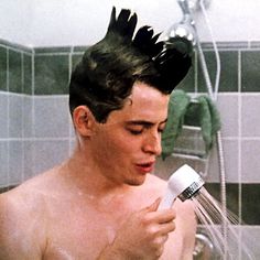 a shirtless man is holding a hair dryer and spraying water on his head