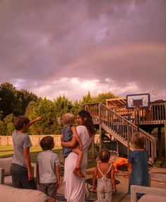 a group of people standing around each other in front of a house under a rainbow