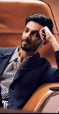 a man sitting in a chair with his hand on his head and looking at the camera