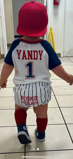 a toddler wearing a red and white baseball hat is walking on the tile floor