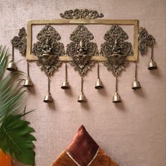 an ornate metal wall hanging with bells and other decorations on the wall next to a potted plant