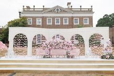 an outdoor ceremony setup with pink flowers and greenery on the stage in front of a large brick building