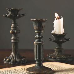 three metal candlesticks sitting on top of an open book next to each other