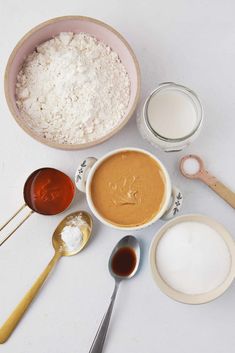 bowls and spoons filled with different types of food on top of a white table