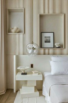 a white bed sitting next to a wall with pictures on the wall and a lamp hanging above it