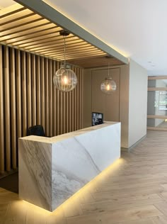 a reception area with marble counter top and lights hanging from the ceiling, along with wooden slats