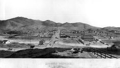 an old black and white photo of a town with mountains in the backgroud