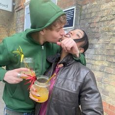 a man and woman standing next to each other with drinks in their hands on the street