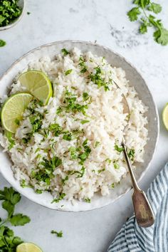 a white bowl filled with rice and garnished with cilantro next to limes