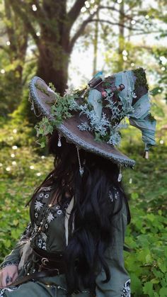 a woman with long black hair wearing a hat in the grass and flowers on her head