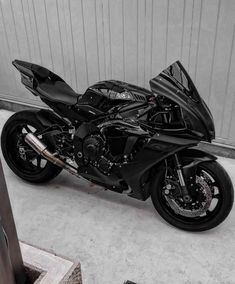 a black motorcycle parked in front of a garage door next to a metal wall and stairs