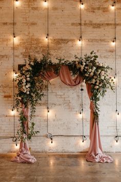 the wedding arch is decorated with flowers and greenery, along with fairy lights hanging from the brick wall