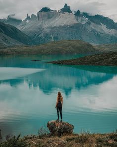 a woman standing on top of a rock next to a lake