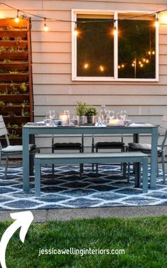 an outdoor dining table and chairs in front of a house with string lights strung over it