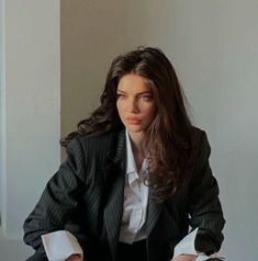 a woman sitting on top of a bed next to a white wall and wearing a suit