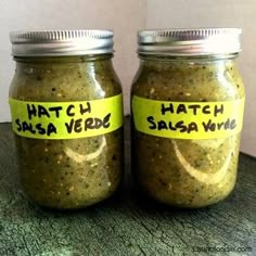 two jars filled with green salsa sitting on top of a table