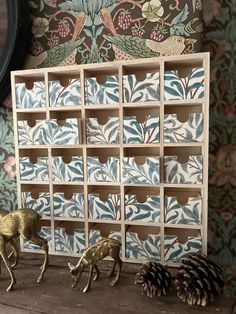 two deer figurines sitting next to each other on a wooden shelf with blue and white wallpaper