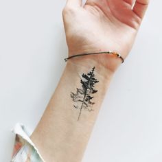 a woman's arm with a small pine tree tattoo on the left side of her wrist