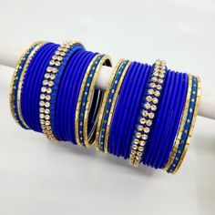 Bangle set comes with 2 sets - 1 per arm. Step into a realm of regal charm with our stunning royal blue bangles, accompanied by a captivating centre thread bangle adorned with diamond zircon stones. The deep and lustrous royal blue hue exudes a sense of grandeur and sophistication, making a bold statement wherever you go. The centre thread bangle adds a touch of artistry and delicacy, beautifully enhanced by the glistening diamond zircon stones, which add a mesmerizing sparkle to the ensemble. E Blue Bangle Bracelet For Wedding, Blue Bangle Bracelets For Wedding, Blue Stone Work Jewelry For Celebration, Blue Bracelets For Festivals, Blue Jeweled Bangle Jewelry, Adjustable Hand Set Bangle For Celebration, Adjustable Hand-set Bangle For Celebrations, Blue Round Jewelry For Festive Occasions, Blue Hand Set Jewelry For Festive Occasions