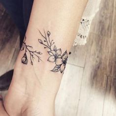 a woman's wrist tattoo with flowers and leaves on her left hand, in black ink