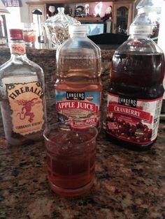 three bottles of apple juice sitting on top of a counter next to a glass filled with ice