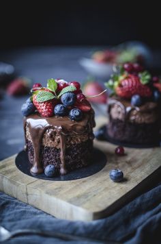 two cakes with chocolate frosting and fresh berries on top are sitting on a cutting board