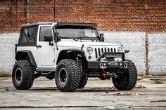 a white jeep is parked in front of a brick wall with black rims on it