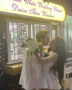 a man and woman standing next to each other in front of a sign that reads private white wedding chapel drive thru window