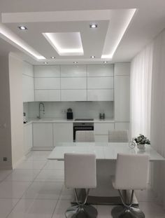 a kitchen with white walls and flooring next to a dining room table surrounded by chairs