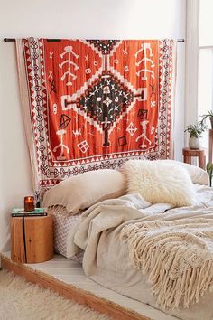 a bed with an orange and white tapestry hanging over it's headboard next to a window