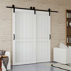 a living room with brick walls and white furniture, two sliding doors open to reveal the bedroom