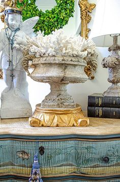 an ornate vase with flowers on top of a dresser next to a wreath and books