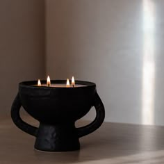 three lit candles in a black bowl on a table